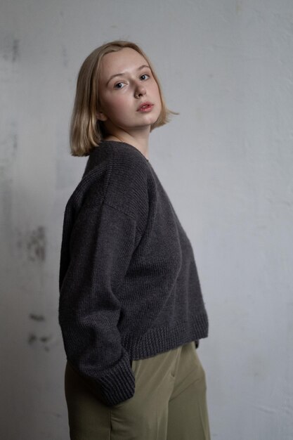 Европейская девушка с короткими светлыми волосами позирует в вязаном свитере для каталога одежды.