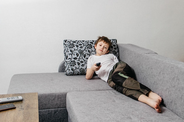 European guy holds a remote control in his hand while lying on a sofa during isolation or a weekend