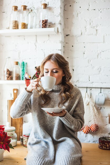 台所に座って、白いマグカップからお茶やコーヒーを飲むヨーロッパ風の女の子