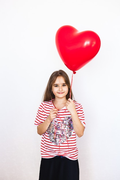 European-looking girl on a white background holding a heart-shaped balloon,
