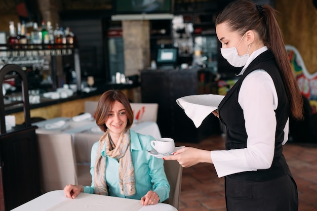 A European-looking waiter in a medical mask serves coffee.