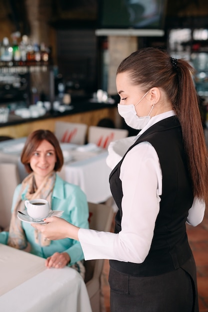 A European-looking waiter in a medical mask serves coffee.