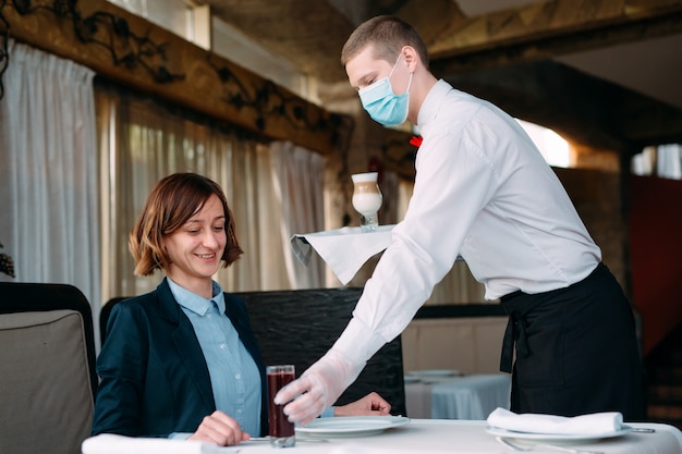 European-looking waiter in a medical mask serves Latte coffee.