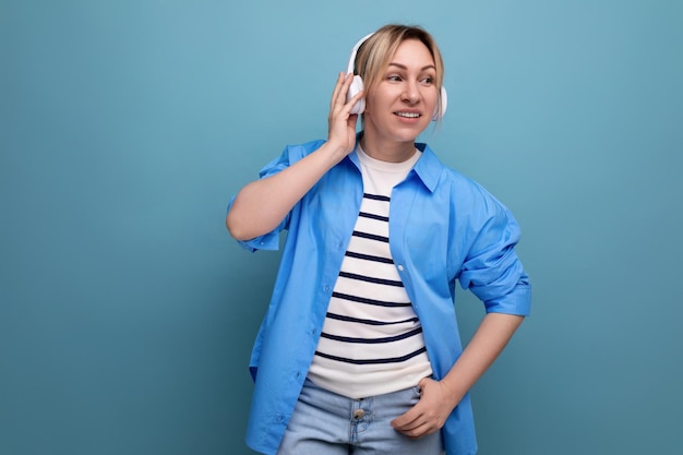 European lovely blond woman in shirt enjoying music in wireless headphones on blue background