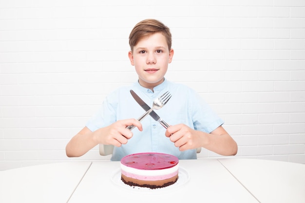 Европейский подросток на белом фоне со столовыми приборами хочет съесть торт