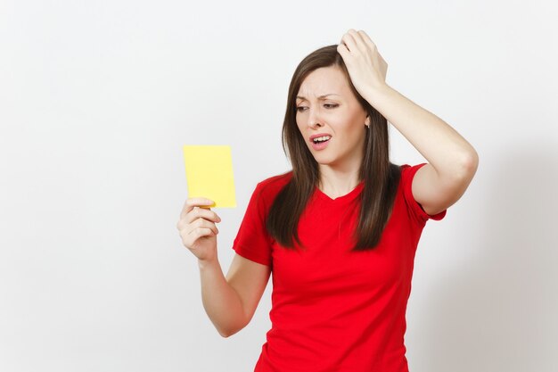 European upset crying shocked young woman, football fan or player in red uniform hold yellow soccer card for retire from field isolated on white background. Sport, play, healthy lifestyle concept.