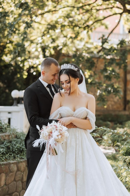 European wedding couple in the park The bride in a beautiful dress with a long train and sleeves Groom in a classic suit