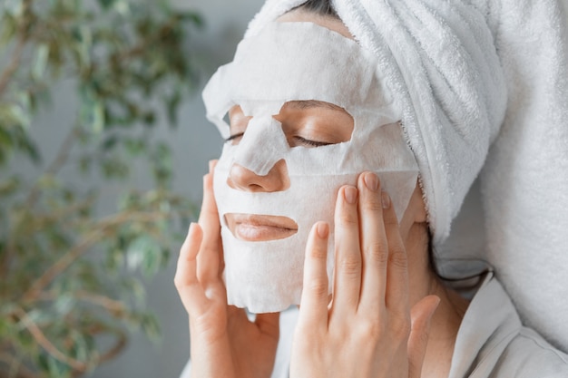 European woman applies white cloth moisturizing mask on her face facial skin care and spa treatments