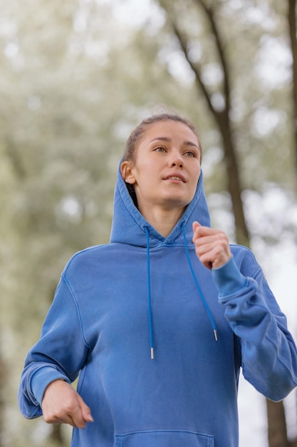 青いパーカーを着たヨーロッパの女性が、公園のフィットネスや屋外でのヨガで走ったり、スポーツをしたりしています。