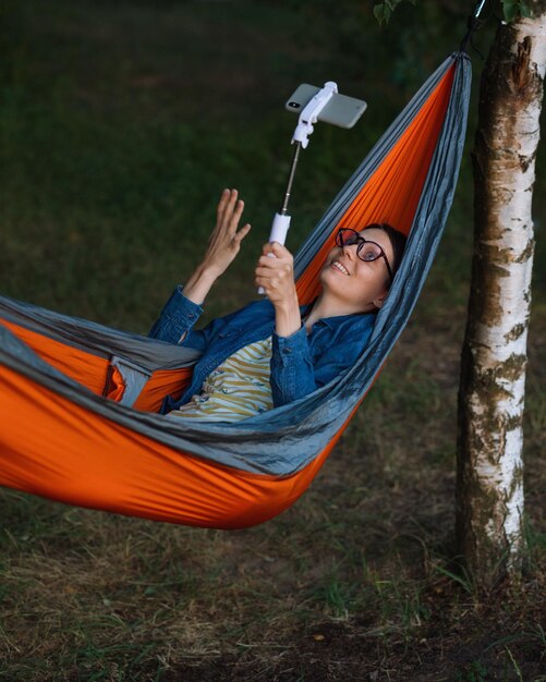 A european woman in a hammock in nature speaks via video link with a webcam a female travel blogger