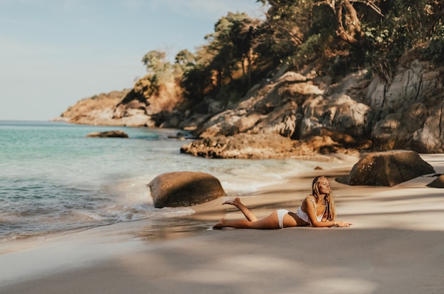 European woman in white bikini swimsuit posing in the beach