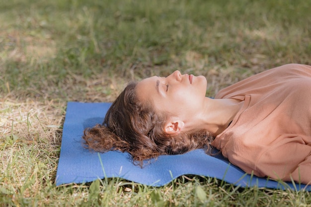 Una donna europea con medita nel parco con il suo cane su un tappetino da yoga blu shavasana e meditazione