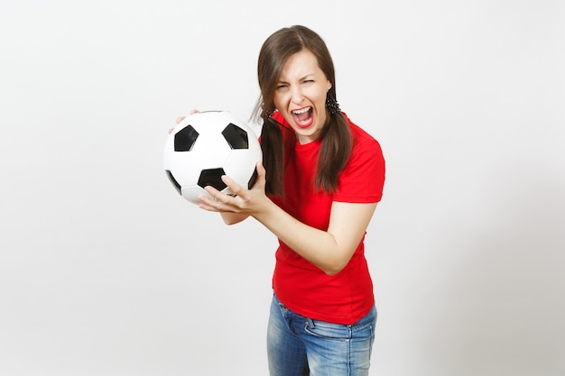 European young crazy angry screaming woman, two fun pony tails, football fan or player in red uniform holding soccer ball isolated on white background. Sport play football, healthy lifestyle concept.