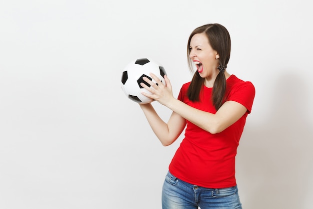 ヨーロッパの若い狂気の怒っている叫び声の女性、2つの楽しいポニーの尾、サッカーファンまたは白い背景で隔離のサッカーボールを保持している赤い制服を着たプレーヤー。スポーツプレーサッカー、健康的なライフスタイルのコンセプト。