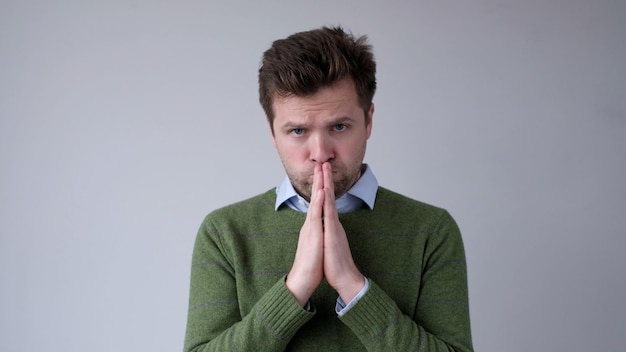 Photo european young man asks for help holds palms together