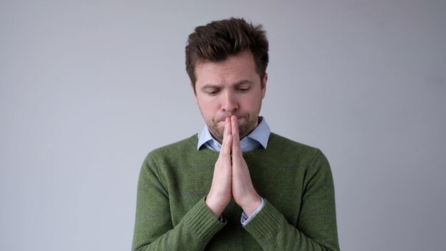 Photo european young man asks for help holds palms together