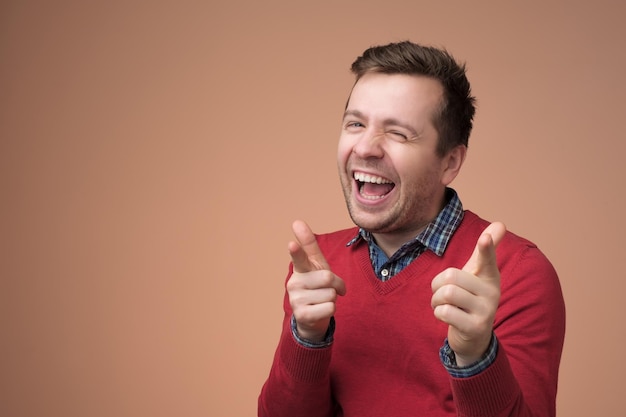 Европейский молодой человек в красном свитере смеется над смешной шуткой