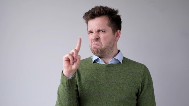 Photo european young man shakes his head in disagreement and says no pointing his finger upwards