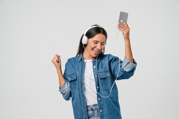 European young woman girl dancing singing listening to the music podcast song singer sound track ebook in headphones earphones on cellphone isolated in white background