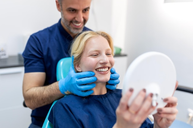 Giovane donna europea sorridente mentre si guarda allo specchio nella clinica odontoiatrica colpo di una giovane donna che controlla i suoi risultati nell'ufficio del dentista