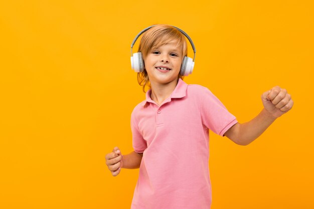 Europese blonde jongen in een roze T-shirt luistert naar muziek in witte koptelefoon op oranje met kopie ruimte