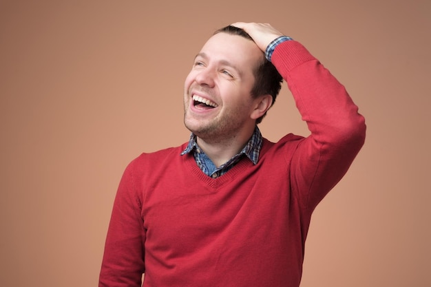 Europese jonge man in rode trui lachen om grappige grap