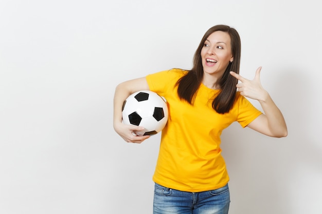 Europese jonge vrouw, voetbalfan of speler in geel uniform met voetbal wijzende wijsvinger opzij geïsoleerd op een witte achtergrond. Sport, voetbal, gezondheid, gezond levensstijlconcept.