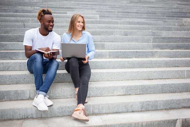 Europese jonge vrouwelijke en Afro-Amerikaanse mannelijke studenten die op trappen in het park zitten