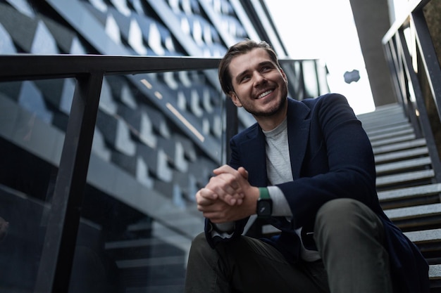 Europese lachende freelance man zittend op de trappen van een gebouw op straat