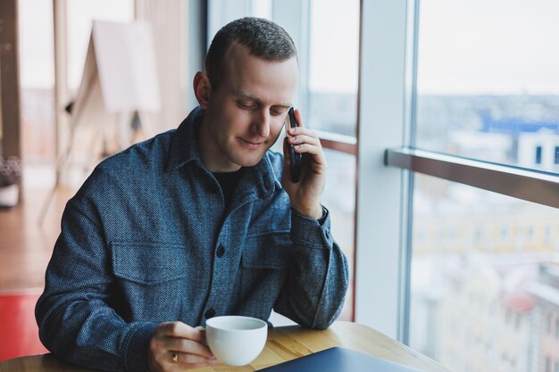 Europese mannelijke freelancer bij het controleren van meldingen op smartphone over geldtransacties die online zaken doen, op afstand werken in café en koffie drinken