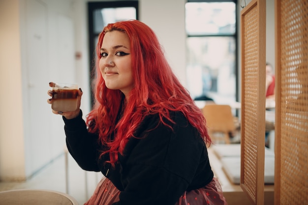 Europese plus size vrouw jong rood roze haired lichaam positief meisje zit in café met koffiedrank