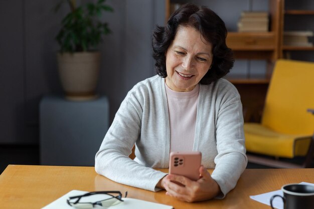 Europese senior vrouw van middelbare leeftijd met behulp van smartphone-aanraakscherm typen scroll-pagina stijlvol o