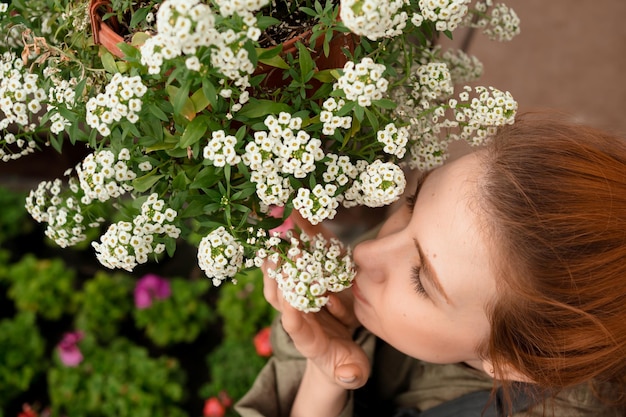 Europese vrouw met rood haar en gesloten ogen knuffelen en snuiven van witte bloemen in de tuin in de zomer