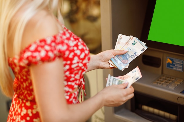 ユーロ紙幣とATM機がクローズアップ。屋外の現金自動支払機からユーロのお金を取る女性。ユーロ紙幣と女性の手