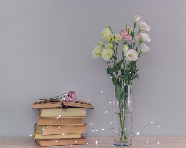 写真 ユーストマの花の花束、古いヴィンテージの本と花輪のライトのスタック。コンセプトを読んでリラックスしてください。