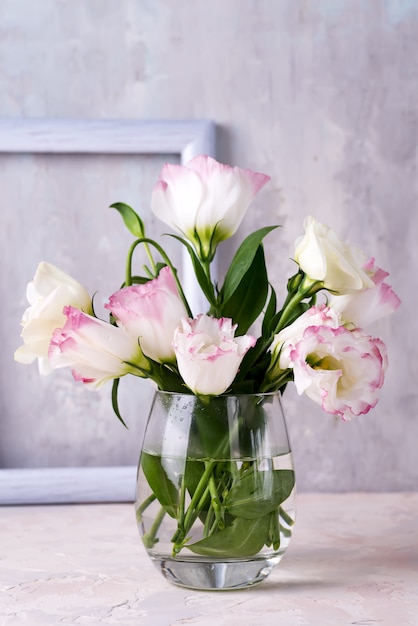 Eustoma flowers in vase on table near stone wall.