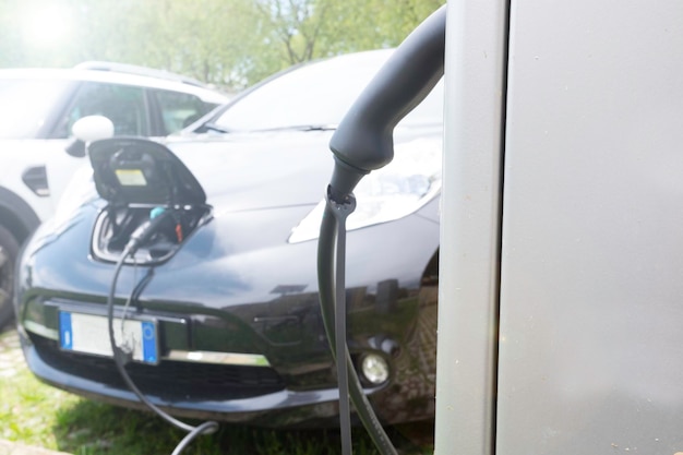 Ev car or electric car at charging station with the power cable\
supply plugged in on blurred nature with sun light background\
ecofriendly alternative energy concept main focus on the right