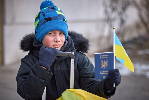 Evacuazione di civili bambino triste con la bandiera dell'ucraina famiglia di rifugiati dall'ucraina che attraversa il confine mano che tiene un passaporto sopra i bagagli con bandiera gialloblu fermare il sostegno alla guerra ucraina