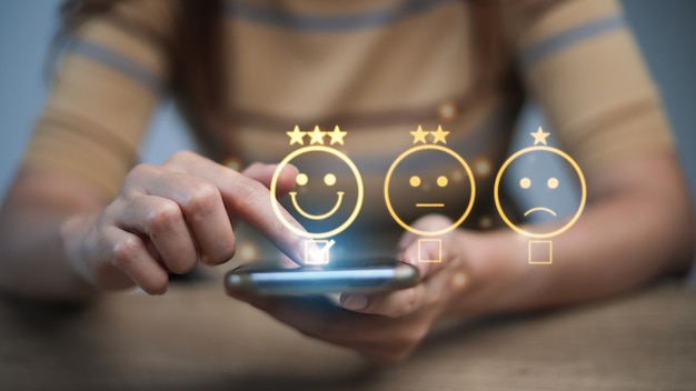 Evaluatieconcept van de klantenservice glimlacht Aziatische vrouw Gebruikt een smartphone En ze drukt tevreden op een emoticon-glimlach op het virtuele touchscreen