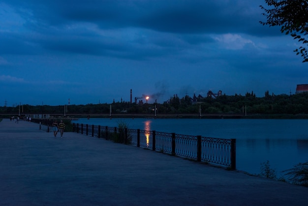 Evening blue landscape of the river on the background of industrial buildings with fire