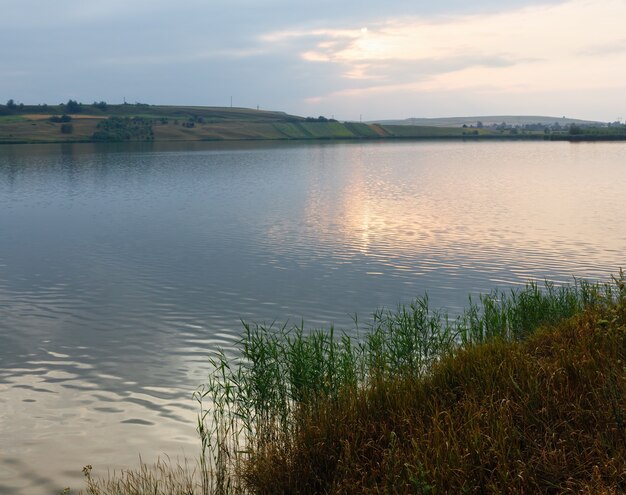 Evening lake scenery with sun reflection on water surface.