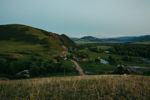 Evening landscape of the village built among the hills, forests and mountains. Open space. Wild nature. Interaction with the nature of Altai.