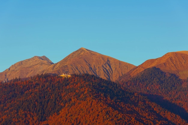 秋の森の斜面にある山の 3 つのピークの夕方の光