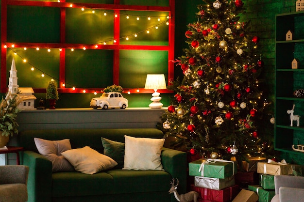 Вечерний новогодний интерьер комнаты. Уютный свет от лампы освещает зеленый диван и елку.