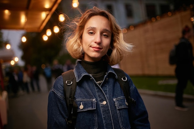 evening portrait of a beautiful young girl dressed in a denim jacket with a backpack