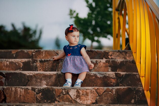 Evening shot of nine months adorable baby sitting on stairs and\
looking at garden lattice