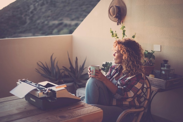 Photo evening with lovely light and beautiful lonelyh woman taking and drinking a tea with old typewriter no technology in front on the table