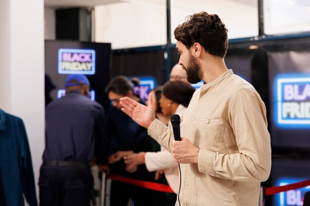 Photo event host holding microphone announces start of black friday sale in modern shopping mall. retail store owner opening clothing store during seasonal holiday sales, welcoming and greeting customers