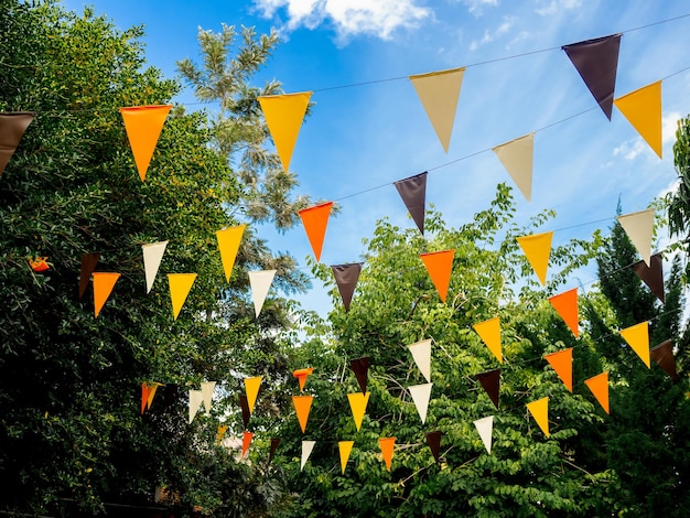 Event outdoor party ornamented with orange yellow brown and
white color tone flags in green garden on blue sky background
colorful triangular flags hanging decorated to celebrate halloween
party