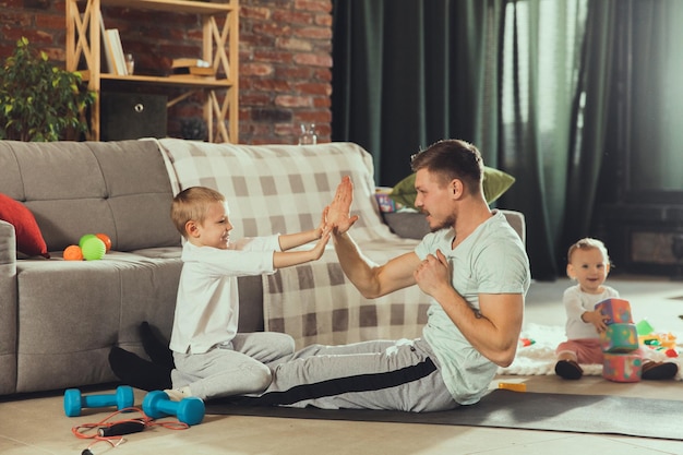 Evenwichtig. Jonge man die fitness, aerobic, yoga thuis, sportieve levensstijl uitoefent. Actief worden terwijl zijn kind op de achtergrond speelt, thuisgymnastiek. Gezondheidszorg, beweging, ouderschapsconcept.